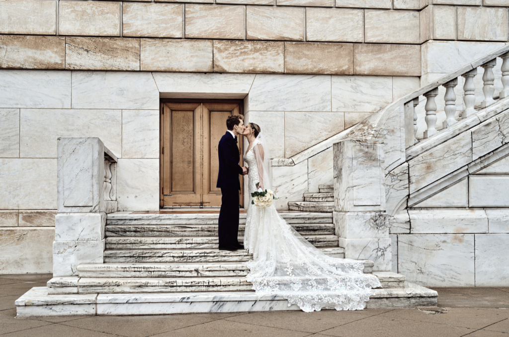 A bride and group stand on the white marble steps on the Detroit Institute of Arts on their wedding day. This is one of the most popular wedding locations in Detroit. Photo taken by Erika Black Photography